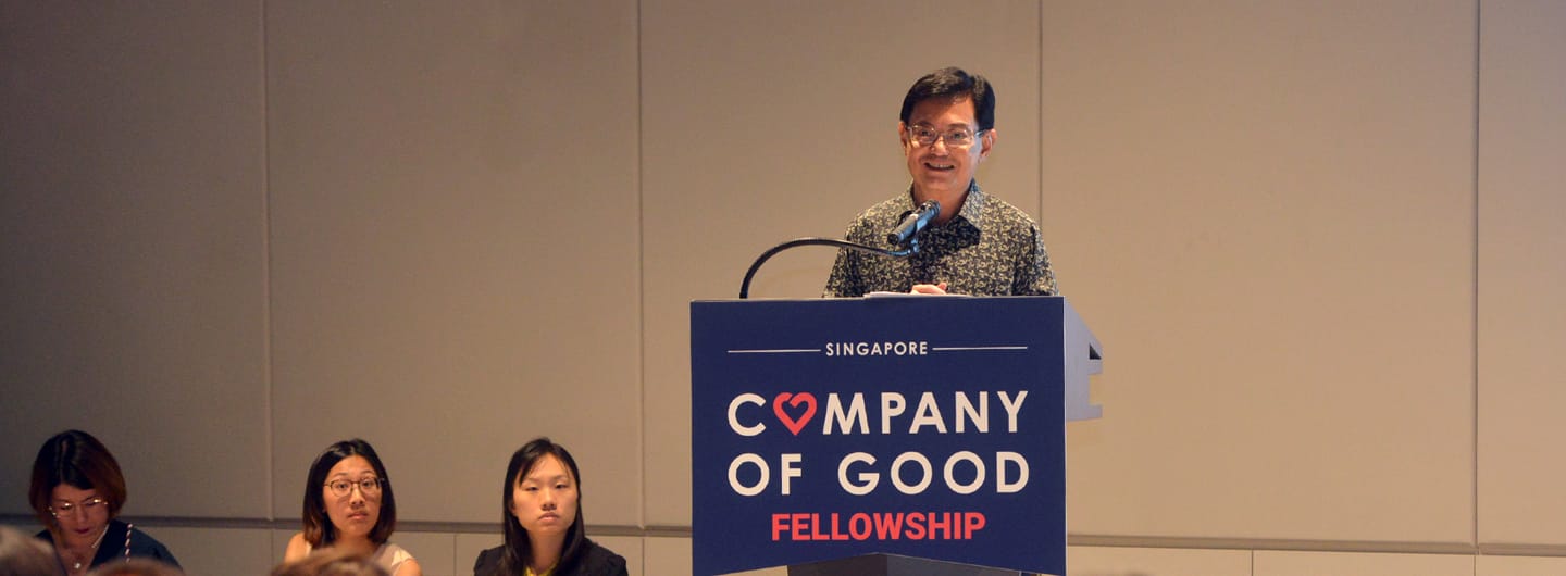 Person at "Company of Good Fellowship" podium, with three people seated at a table.